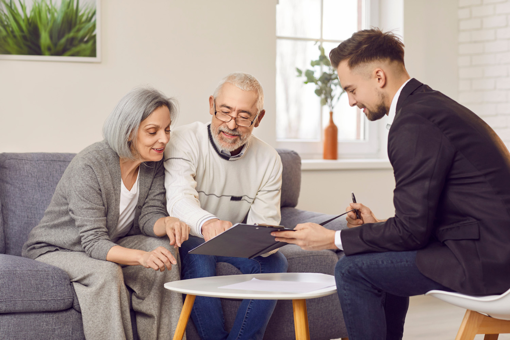 Senior couple reviewing documents with a young advisor at home, smiling and engaged in a discussion.